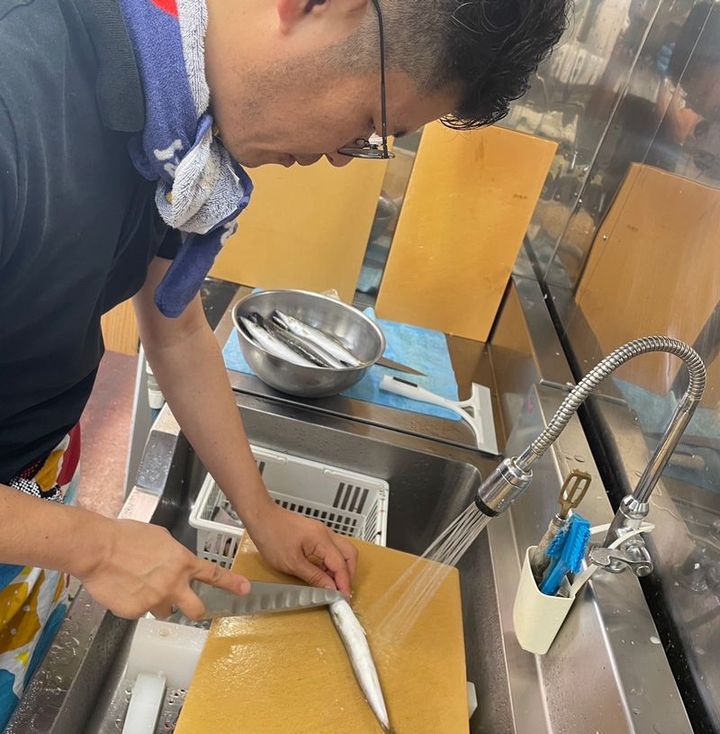 マルカマにてミズカマスの背開きに挑戦中の筆者。魚を常温に長く置くときは氷を当てるように、と上田さんから指導されました。夏場は温度管理が必須です（写真提供＝サカナヤマルカマ）