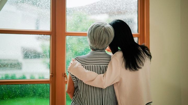 家の窓際で寄り添う女性と彼女の母親