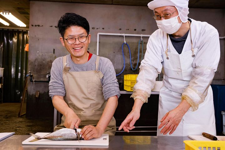 アジの3枚おろしを習う大宮さんと「島源商店」スタッフの鈴木さん