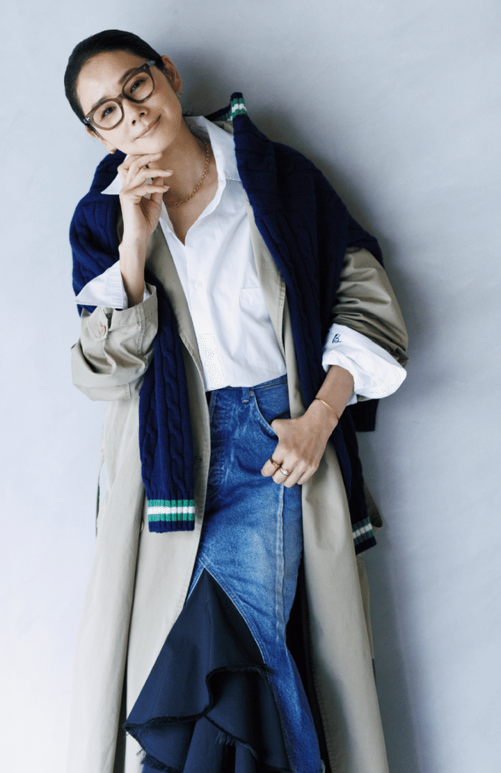 スカート¥209,000、シャツ¥45,100、レンチコート¥242,000 ／すべてマディソンブルー、肩にかけたニット¥39,600 ／スローン（ザ ショップスローン 神戸）、メガネ¥70,400 ／アーレム（グローブスペックス エージェント）、ピアス（右耳）¥66,000、 ピアス（左耳）¥231,000、ネックレ ス¥916,740、バングル¥319,000、 パールのリング（左手中指）¥110,000、 ダイヤのリング（左手中指）¥181,500、リング（左手人差し指）¥668,800／すべてシハラ（シハラ トウキョウ）