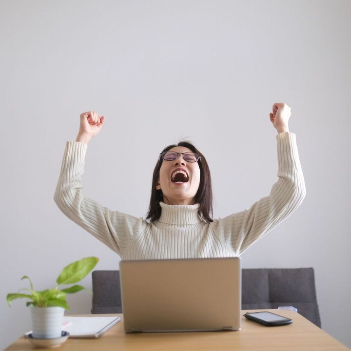いいニュースを聞き両手を上げて喜ぶ女性