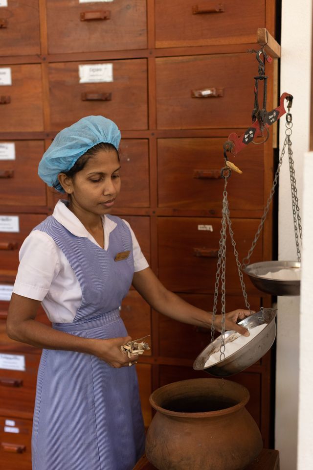 後ろの棚に様々な種類の薬草が並べられていて計量しながら調合します。Photo_ Akiko Ishino
