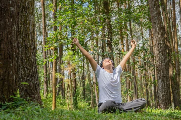 森の中であぐらをかいて座り、両腕を伸ばす男性