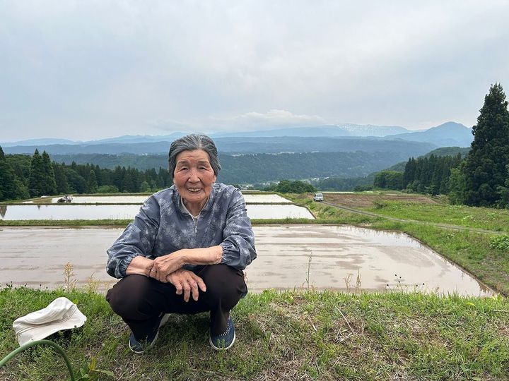 かつて「よそ者の嫁」たち仲間7人で作った山の上の田んぼを背景に微笑む桑原千恵さん