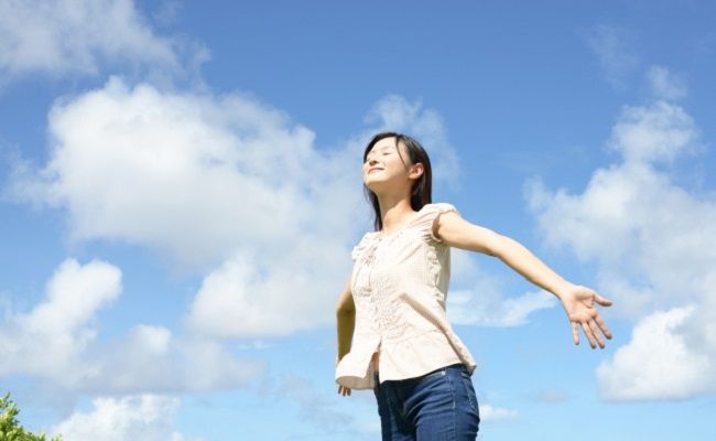 青空の下で両手を広げている女性