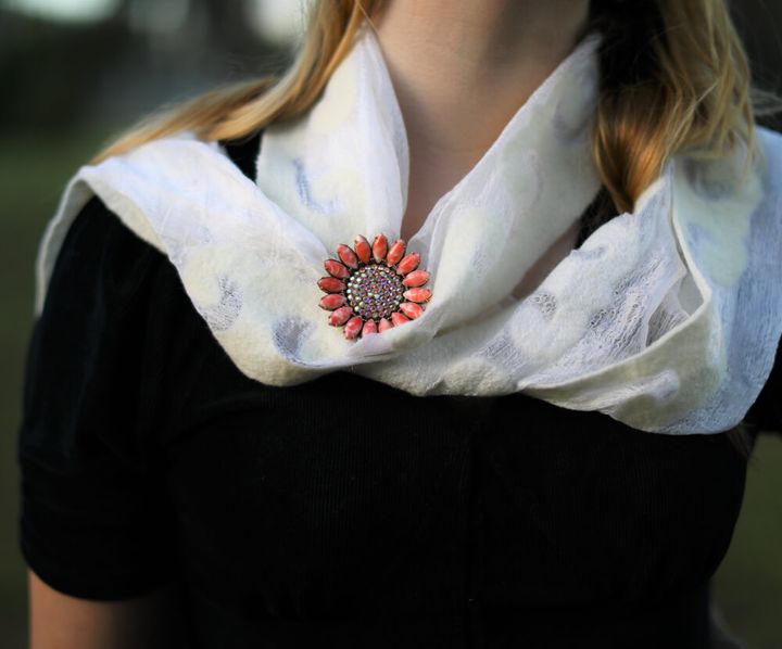 白いストールに赤い花のブローチが付いている