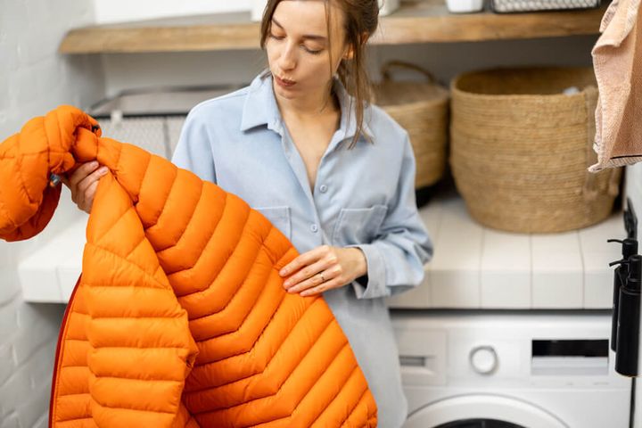 洗濯機の前でダウンジャケットを見る女性