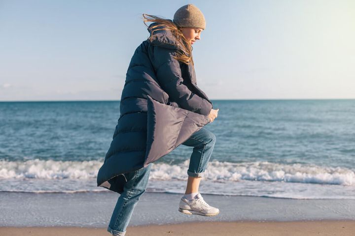 ダウンコートを着て海辺を歩く女性