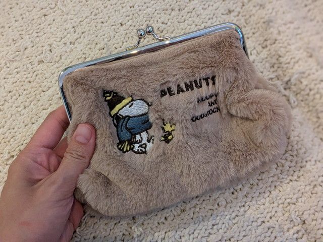 手に持ったスヌーピー ふわもこがま口ポーチ。刺しゅうとふわふわ素材の可愛らしい外観