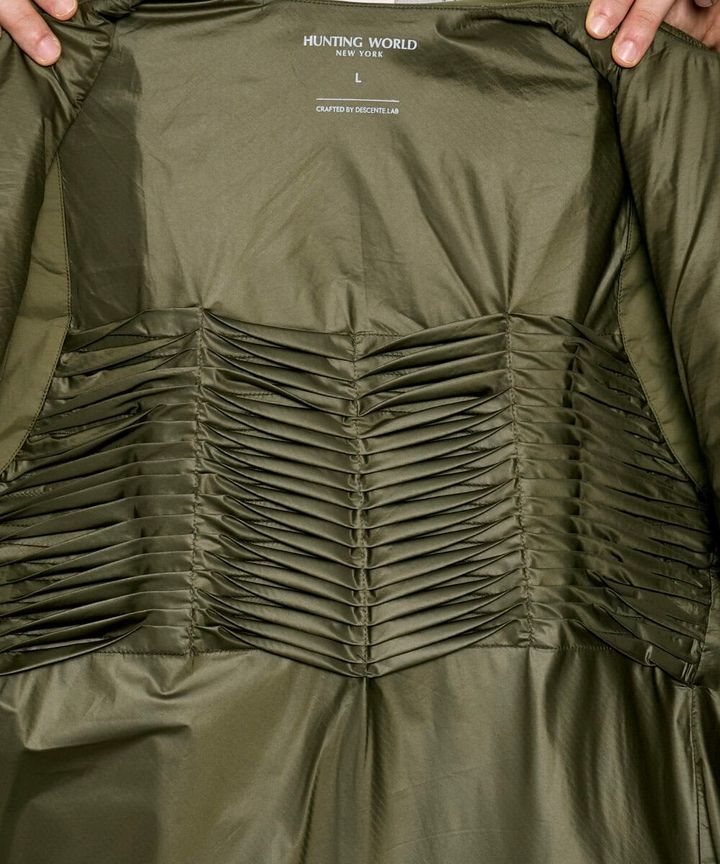 裏地には光の波⻑領域を余すことなく吸収し、熱に変換する保温素材「HEAT NAVI®」を採⽤。クリーンエネルギーである太陽光を効率よく活⽤し、光吸収性能を⾼めた蓄熱保温素材により、従来の未加⼯素材に⽐べて+5℃の発熱効果を発揮。さらに、背中の中央部分にはクロスプリーツを配置し、「HEAT NAVI®」の表⾯積を増やすことで、従来品よりも速暖性が向上。