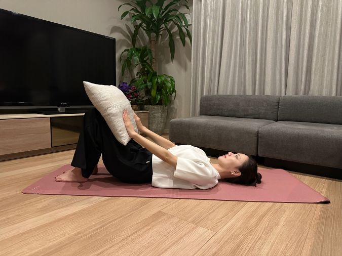 仰向けで両膝を立て、膝の上にクッションを乗せる。