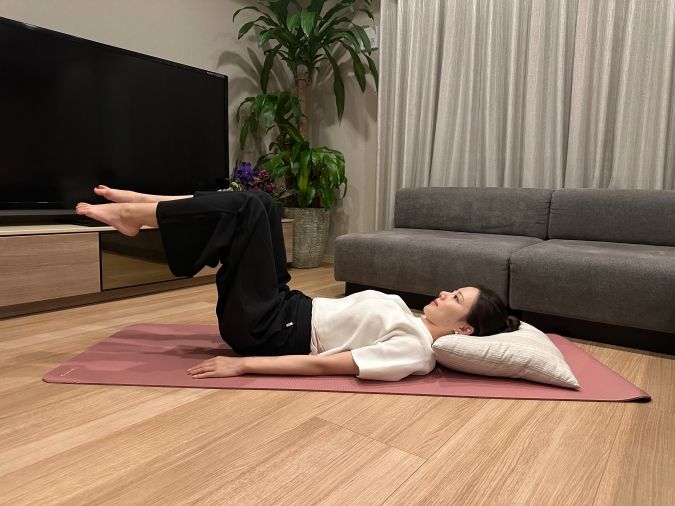 仰向けになって頭の下にクッションを置き、両脚を上げて、膝と股関節を90度に曲げる。（テーブルトップの姿勢）