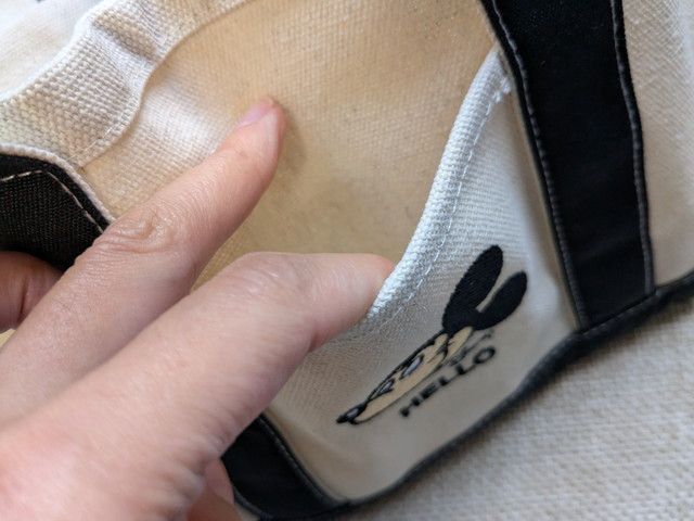 トート前面のポケットに指を入れている様子。外ポケット付きで小物をサッと入れられる