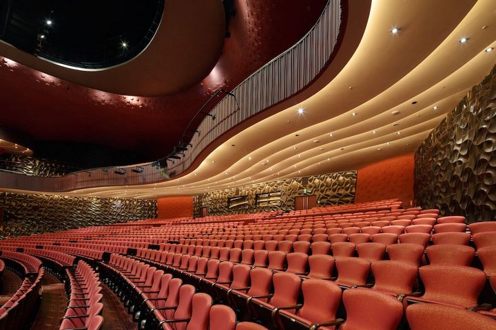 赤を基調とした大劇場。階段状の座席や左右のボックスシートが、3次元曲面から成る空間の中に、舞台を囲むように置かれている。Photo_ Kai Nakamura