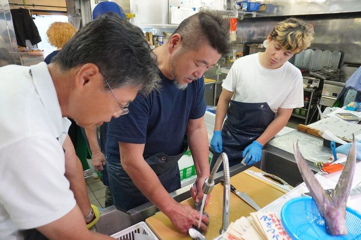 マルカマのスタッフにアナゴのさばき方を指導中の上田さん