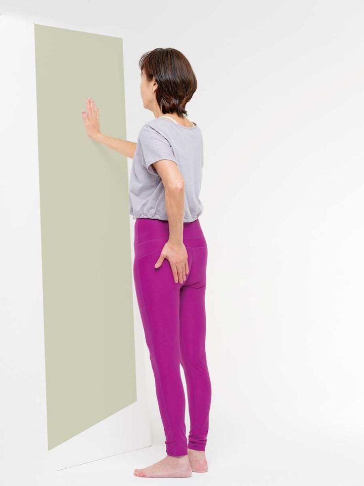 【１】壁を真正面にして、足を軽くそろえて立ちます。右手を壁につき、左手を左のお尻にあてます。