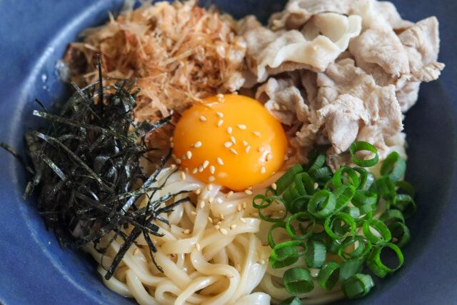 真ん中に卵黄をのせて、豚肉、かつお節、万能ねぎ、刻み海苔をまわりにトッピングし、白いりごまをふって、ラー油と酢をお好みでまわしかける。