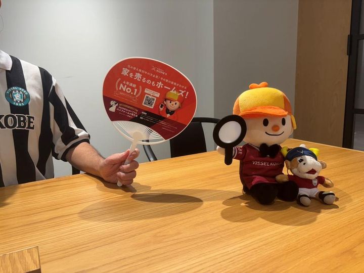 画像: 神戸サポーター向けに配布しているうちわ、ぬいぐるみ。うちわの裏側にはヴィッセル神戸の選手たちの姿が（筆者撮影）