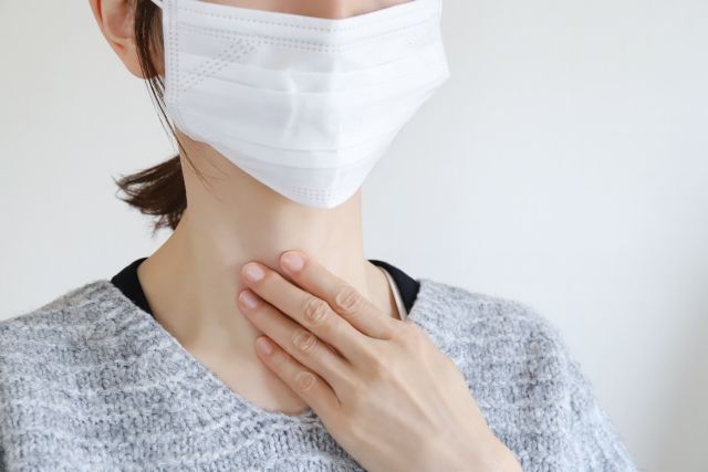 マスクして喉を抑える女性