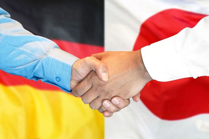 ドイツと日本の国旗を背景に握手を交わすビジネスマン