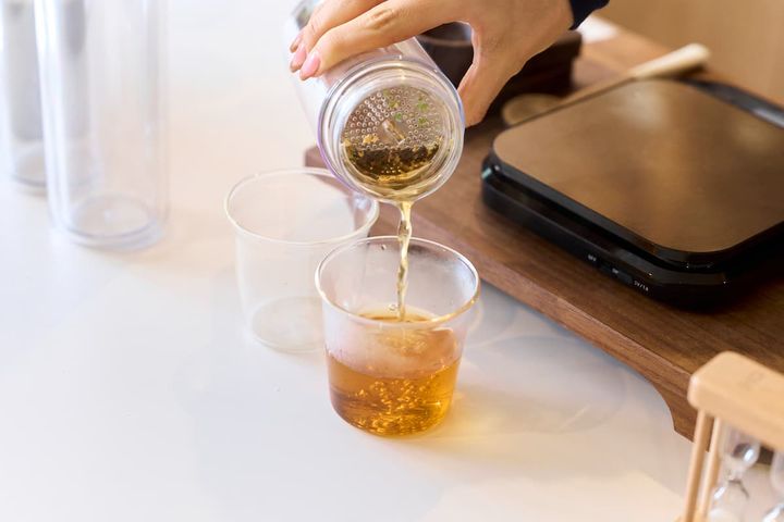 急須ボトルからコップにお茶を注いでいる