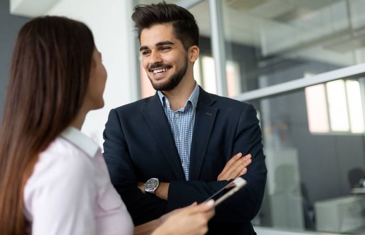 立ちながら同僚の女性と話す笑顔の男性