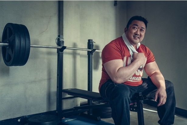 ドンソクがトレーニングマシンに腰かけ笑顔を見せる様子 [c]2025 LOTTE ENTERTAINMENT & BIG PUNCH PICTURES & NOVA FILM AllRights Reserved.