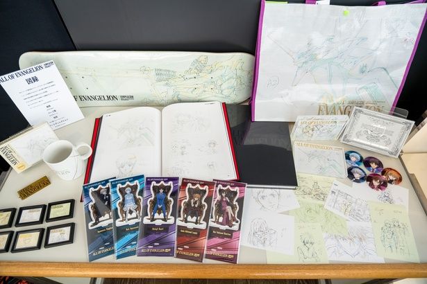 会場限定の主なオフィシャルグッズ。缶バッジセット(2750円・右)、展示原画をあしらったトレーディングマグネット(660円・左下)、スケートボードデッキ(1万4850円・左上)、40枚入りのポストカードBOX(7700円・右下)など魅力的なアイテムがそろう