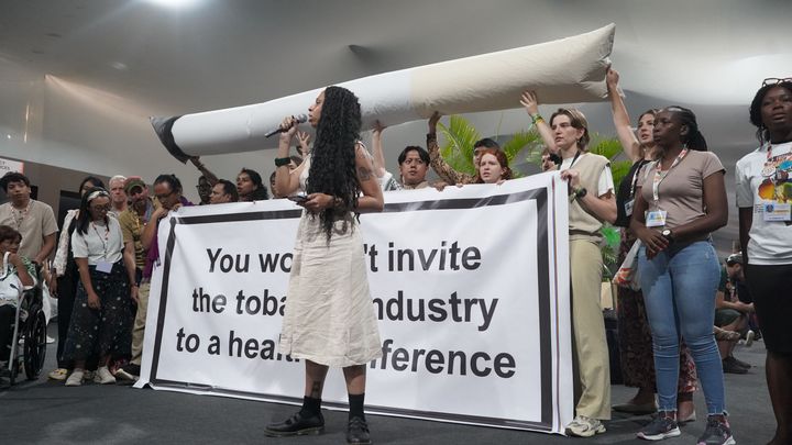 COP30会場内にて、「健康問題の会議であれば、タバコ産業のロビイストは招待しないはず」というバナーを掲げ抗議を行う団体。