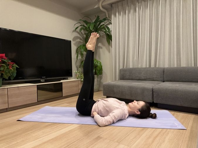 仰向けになり、両脚を天井方向に向かって伸ばす。つま先を少し外に開き、かかと同士を軽く寄せてVの字を作る。両手はお尻と腰の間に入れ、下腹を引き締める。