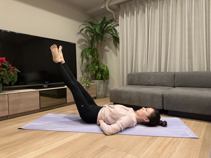 （2）息を吐きながら、両脚を30度下ろす。この時、脚の重さをお腹で支えるイメージで腰が反らないように、両手を押すようにお腹に力を入れる。