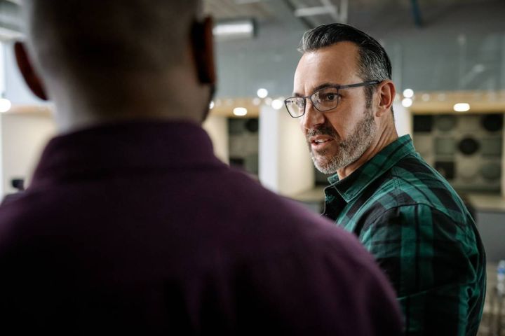 険しい表情で同僚と話す男性