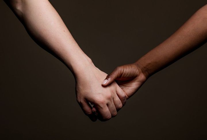 白い肌の腕と黒い肌の腕が手をつなぐ様子