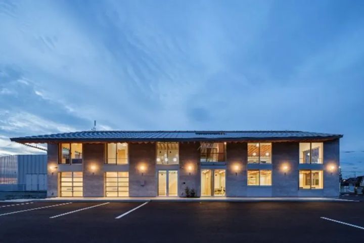 モダンなデザインの建物。駐車場があり、夜空の下でライトアップされている。