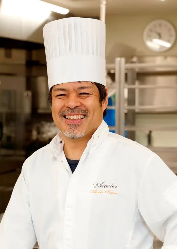 シェフの男性のポートレート。彼は白いコック帽と制服を着て笑顔で立っている。