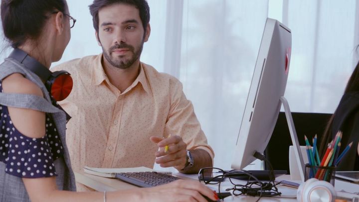 同僚の女性とデスクで話し合う男性