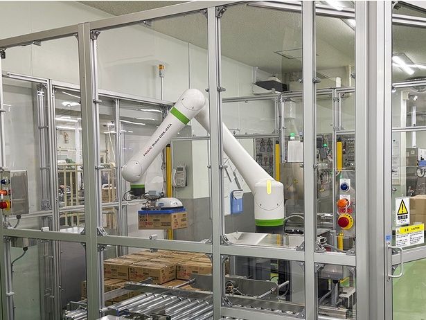 白い大きなアームが、パウチの梱包された段ボール箱を積み重ねていく