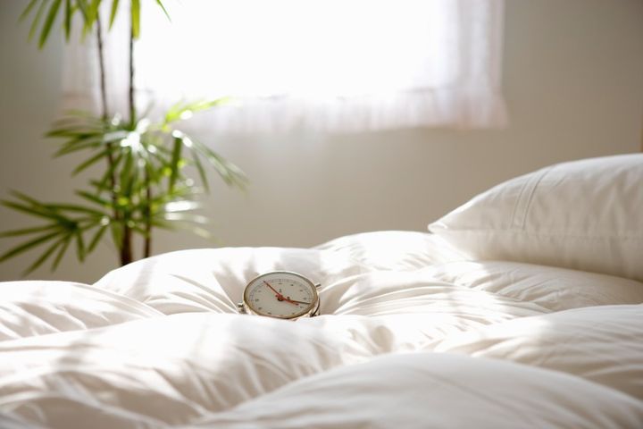 朝日の中のベッドと目覚まし時計 朝起きる