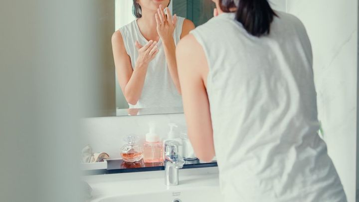 洗面所で顔にクリームを塗っている女性