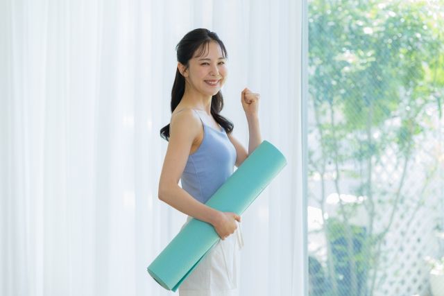 ヨガマットを抱えて笑顔で応援ポーズを作る女性