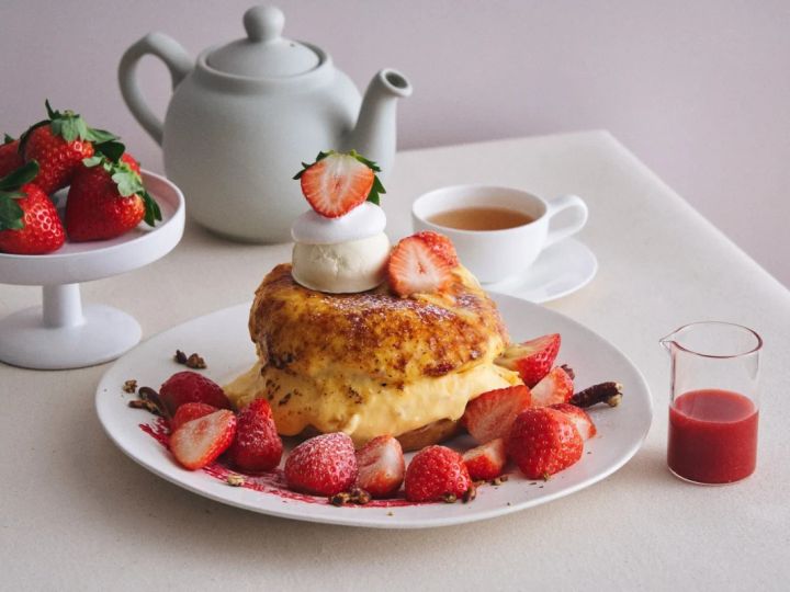 いちごが添えられたパンケーキと紅茶、ティーポットの画像。パンケーキはホイップクリームとアイスクリームで飾られており、皿にはいちご、ナッツ、ソースが添えられています。