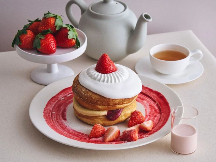 いちごのパンケーキと紅茶のセットの写真。パンケーキはホイップクリームとイチゴで飾られており、皿には赤いソースが塗られている。他に、イチゴ、紅茶、ピンク色の飲み物が写っている。