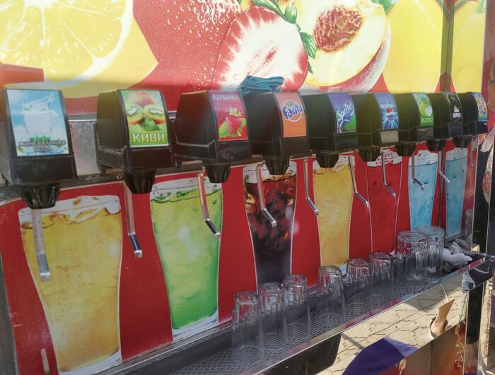 屋台のドリンクサーバーがずらりと並ぶ様子。フルーツ系やコーラ、スプライトなどの炭酸飲料が色とりどりに並び、下にはグラスが用意されている。