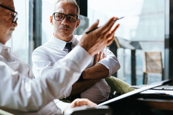 険しい表情で同僚の話を聞く男性