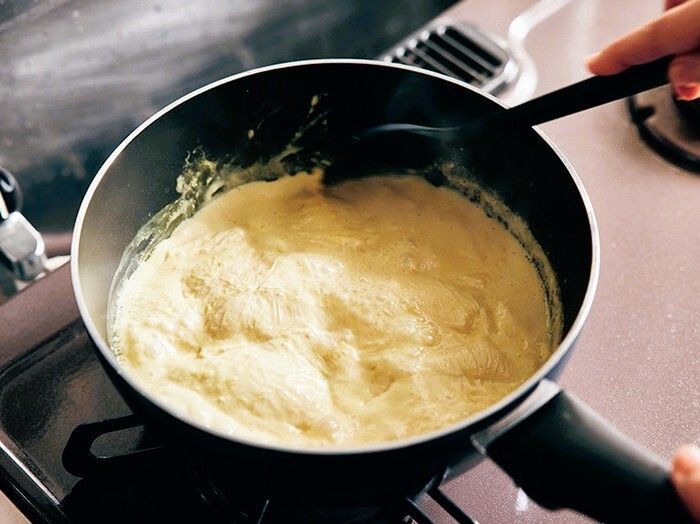 深型フライパンで料理中の様子。滑らかなソースやスープを木べらでかき混ぜる工程。家庭料理や自炊派に人気の万能フライパンは、玄米食や麺料理にもぴったり。忙しい日常の中でも手作りごはんを楽しむライフスタイル。