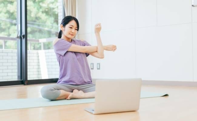 パソコンを見ながらストレッチをする女性のイメージ