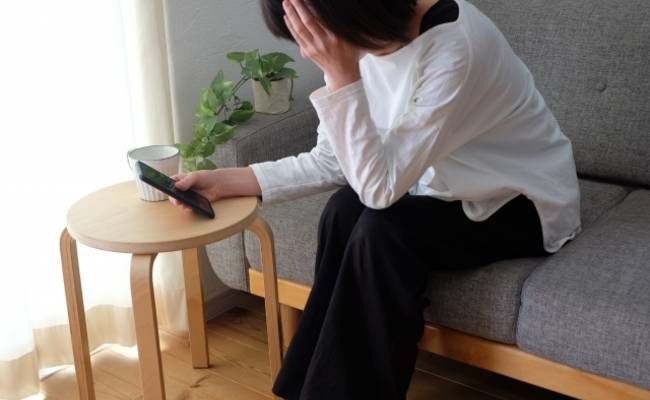 スマホを見て悲しむ女性のイメージ