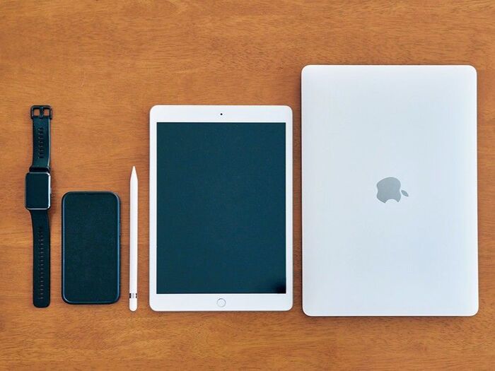 スマートウォッチ、スマートフォン、Apple Pencil、iPad、ノートパソコンが並んだデジタル機器のセット。リモートワークをきっかけにiPadを活用し始めたという、60代女性の“デジタル三種の神器”