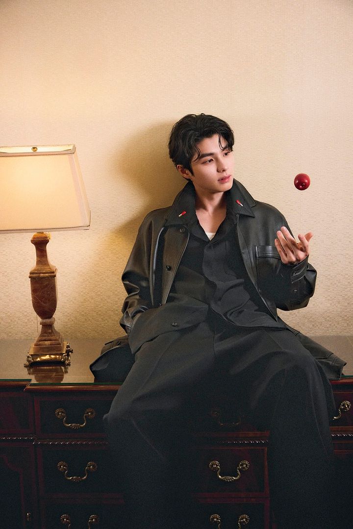 オールブラックのスーツで、宙に浮かぶリンゴを見つめるホリデイ撮影カット