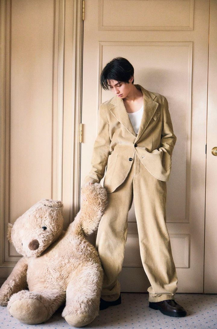 本田響矢がコーデュロイのスーツ姿で、ぬいぐるみに手を伸ばすホリデイ撮影シーン